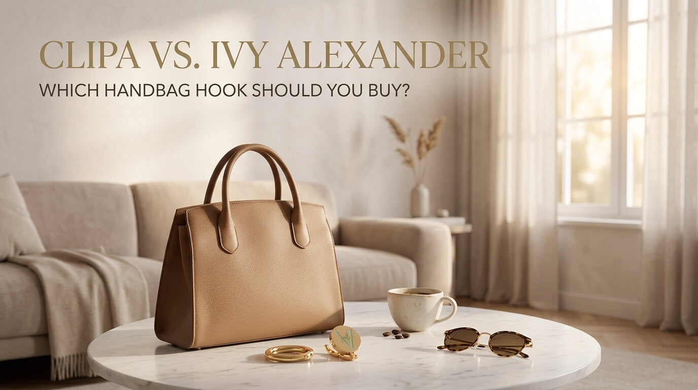 A beige structured leather handbag sitting on a round marble coffee table alongside gold purse hooks, a coffee cup, and sunglasses in a bright living room.