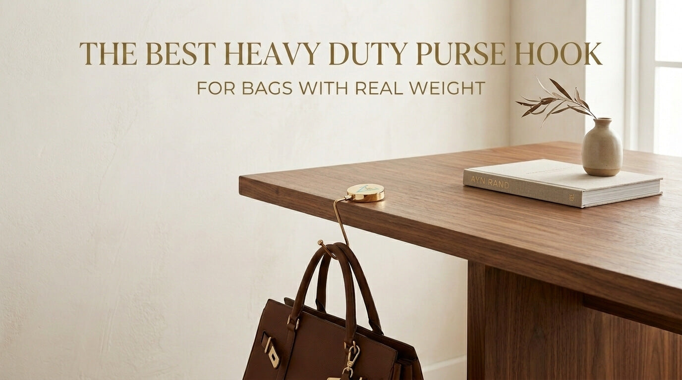 A dark brown leather briefcase hanging securely from the edge of a wooden desk using a sleek, gold purse hook.