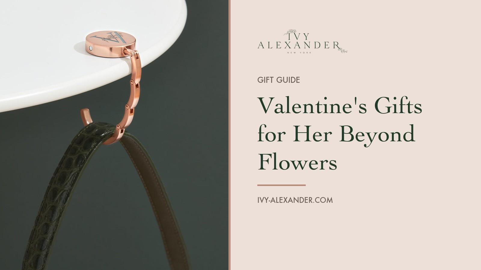 The Ivy Alexander Olivia hook in rose gold hanging a dark green strap from the edge of a white table, beside the title Valentine's Gifts for Her Beyond Flowers.
